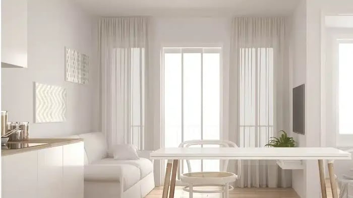 A living room with a white couch, dinner table, and chairs that is clean and organized.